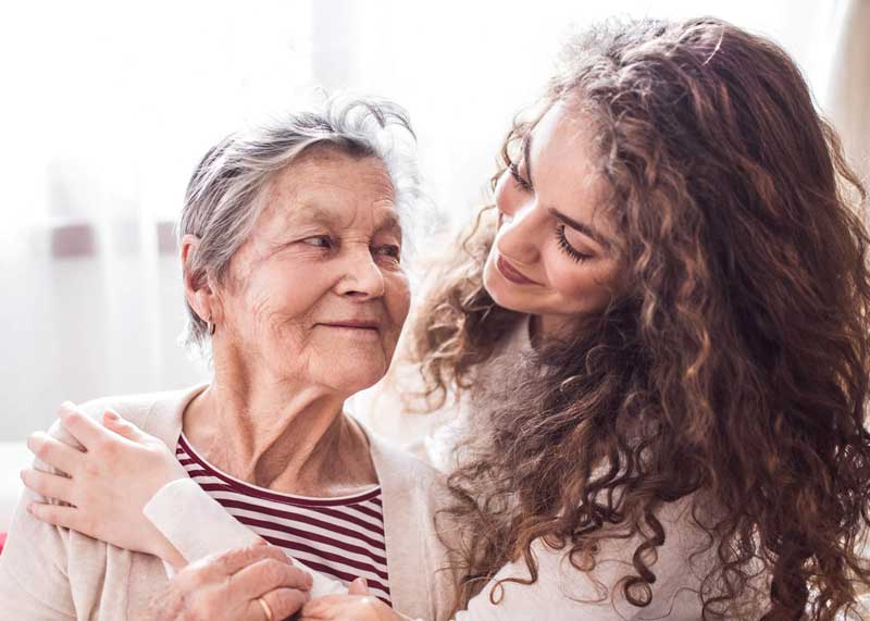 A teenage girl with grandmother at home, hugging.